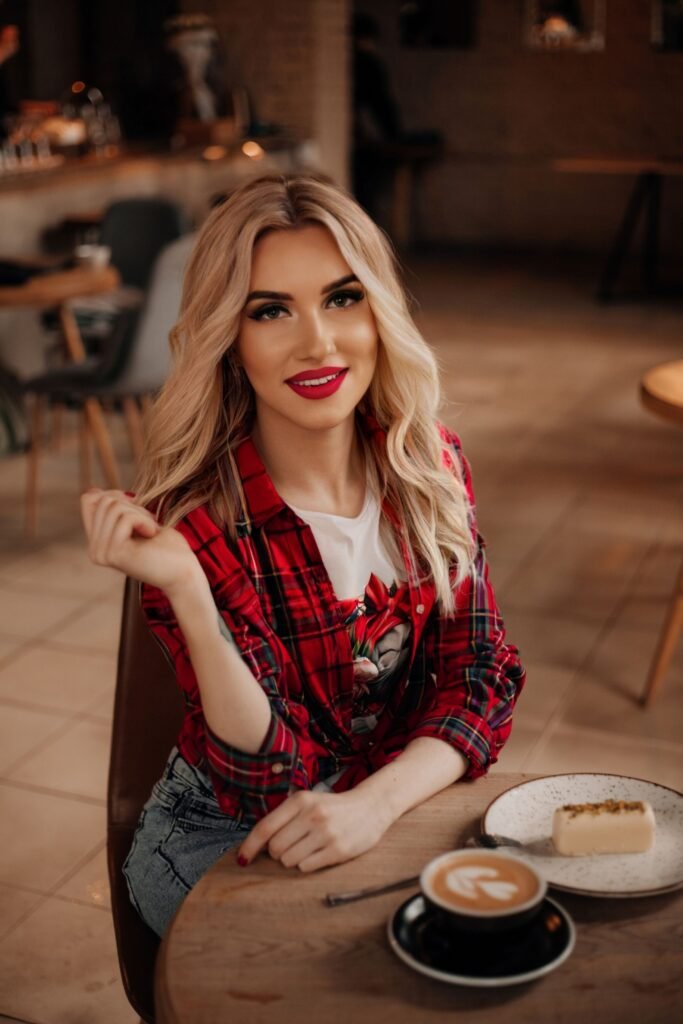Stylish woman in a café with cake and coffee, wearing a red plaid shirt.