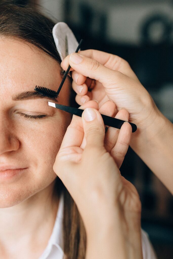 Close-up of a woman receiving professional eyebrow grooming with tweezers.